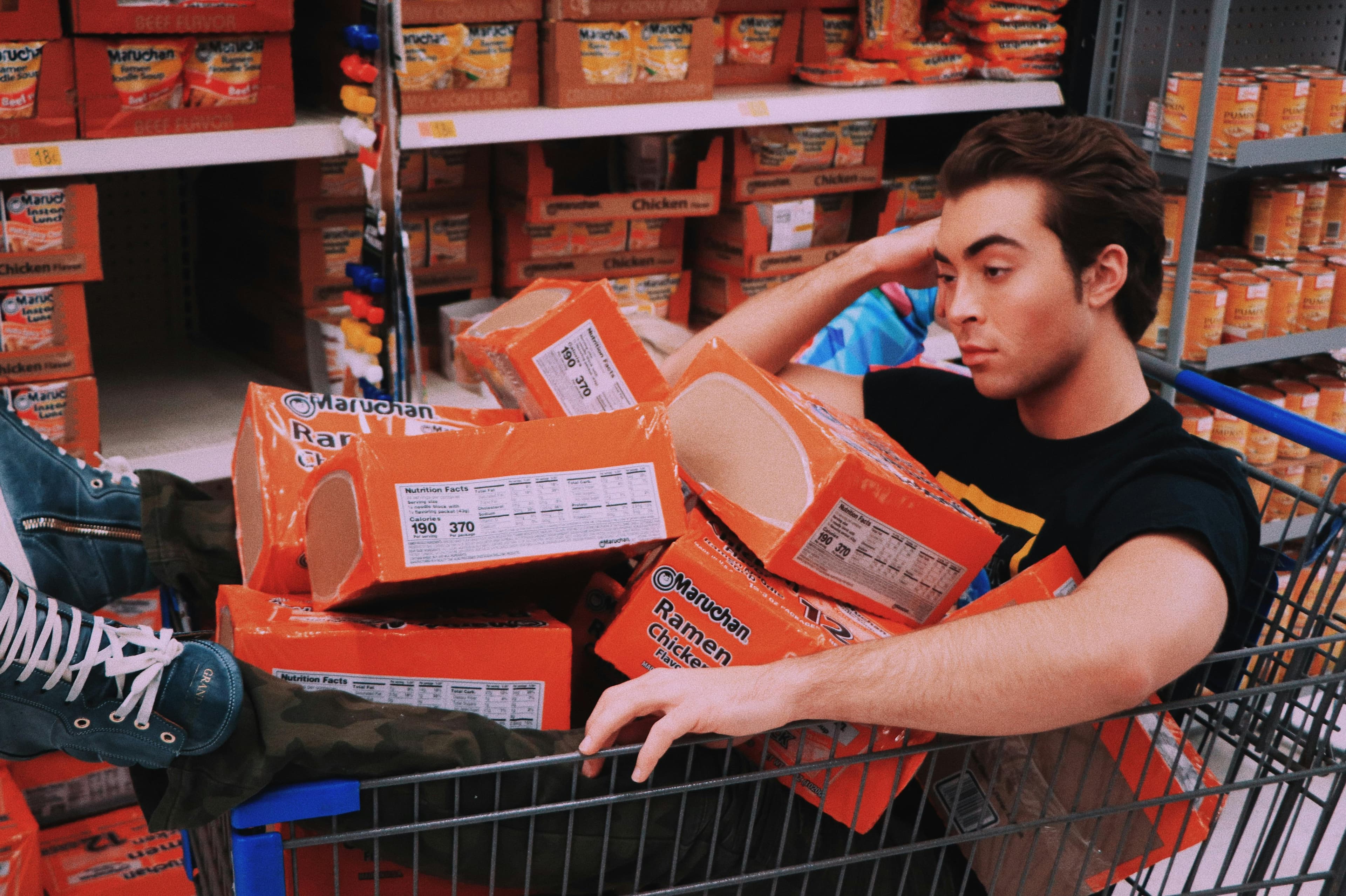 Guy casually sitting in a shopping cart full of groceries.